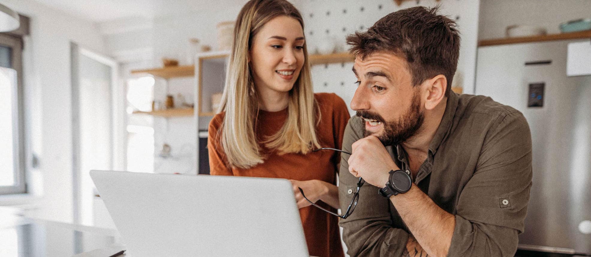 Man and woman are staying in the kitchen, talking and looking at a laptop