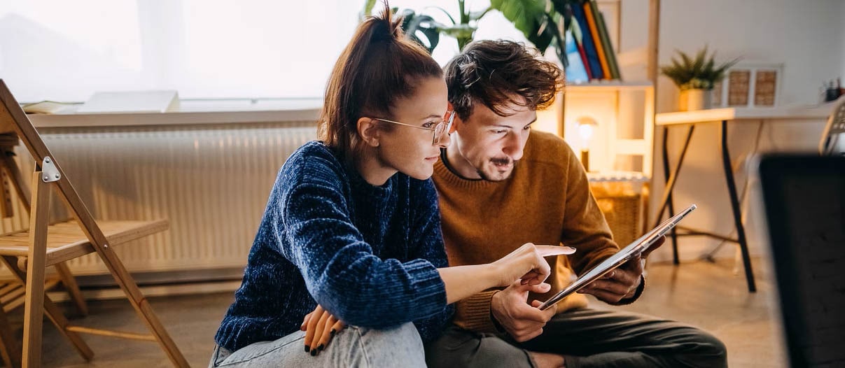 A man and a woman sitting on the floor looking at a device.