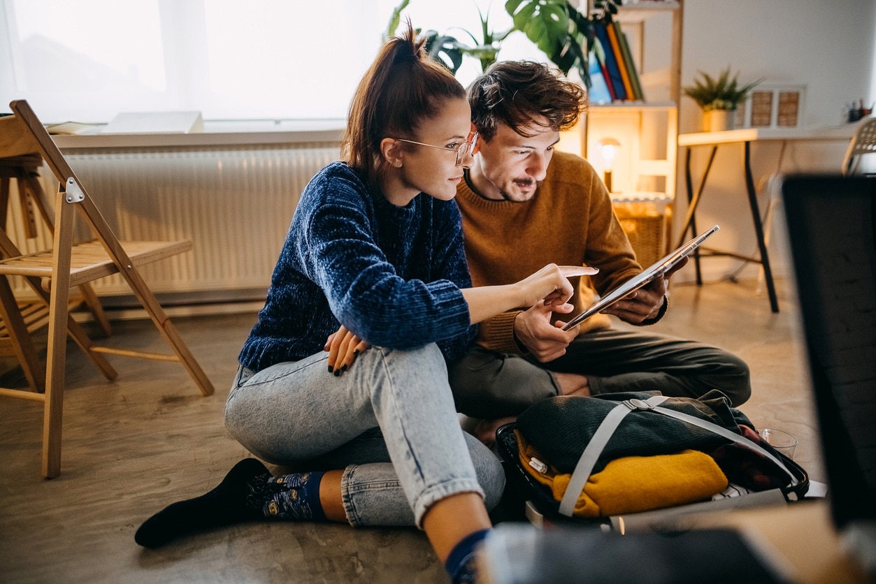 couple sitting on a wooden floor looking at a tablet