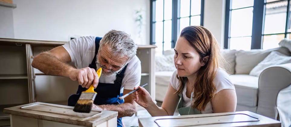 Man and woman are painting drawers of a dresser in a room