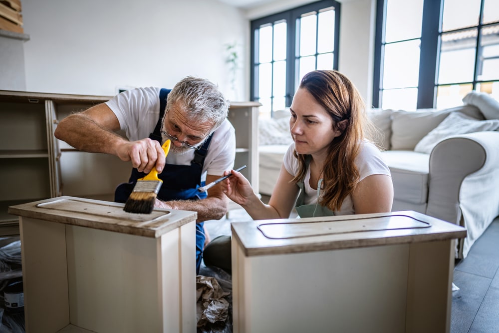 Man and woman are painting drawers of a dresser in a room