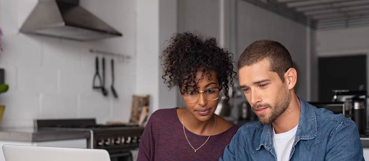 A couple sitting together at a table, using a laptop to pay bills and check their credit score.