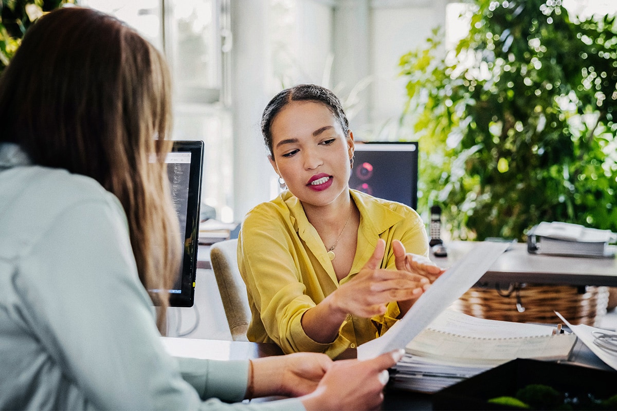 Two women engaged in conversation in an office setting, discussing topics related to closing costs and their implications.