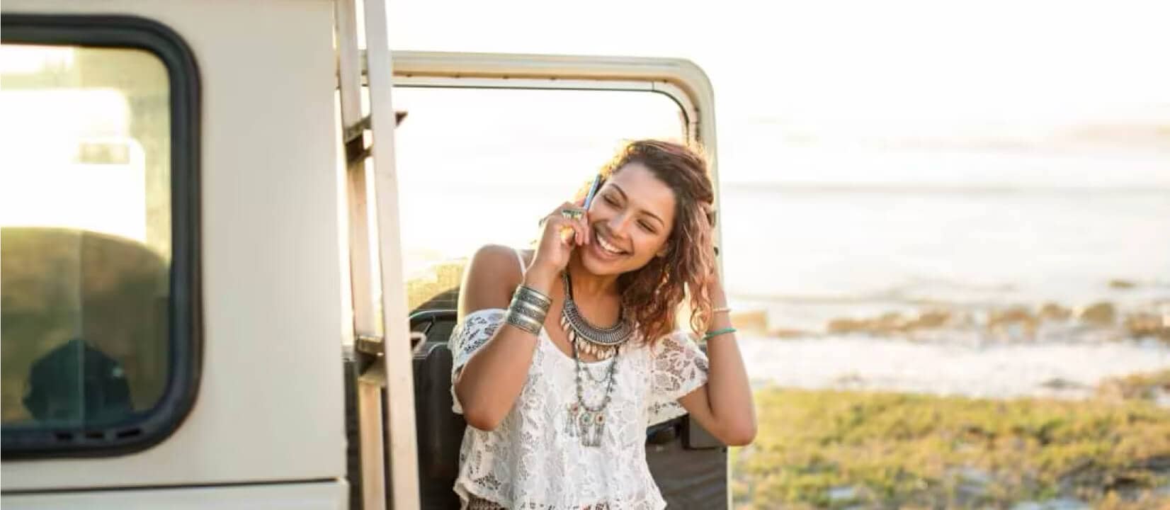 A woman stands beside a car, engaged in a conversation on her cell phone, contemplating car leasing options.