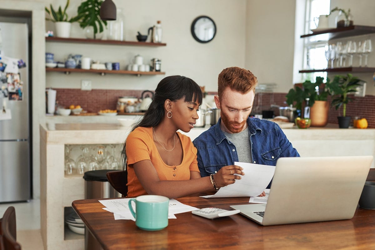 A professional image of a newlywed couple reviewing their finances together on a laptop.