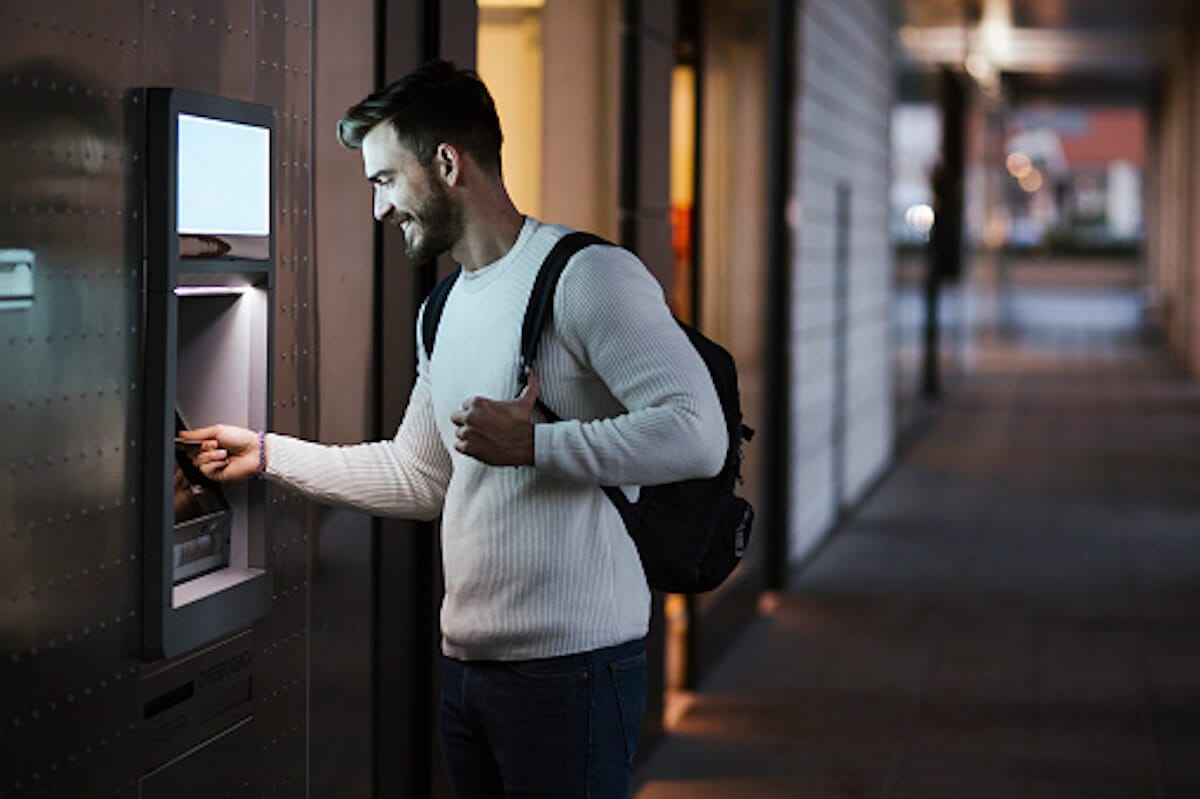 Man is using ATM outside in alley in evening time.