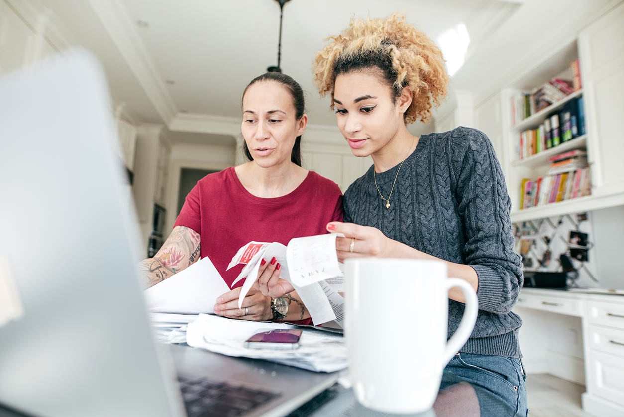 Two women reviewing credit card balance paperwork on a laptop, engaged in discussion and analysis.