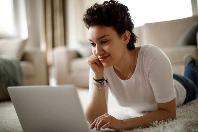 A woman lying on the floor, focused on her laptop as she checks her FICO score for financial insights.