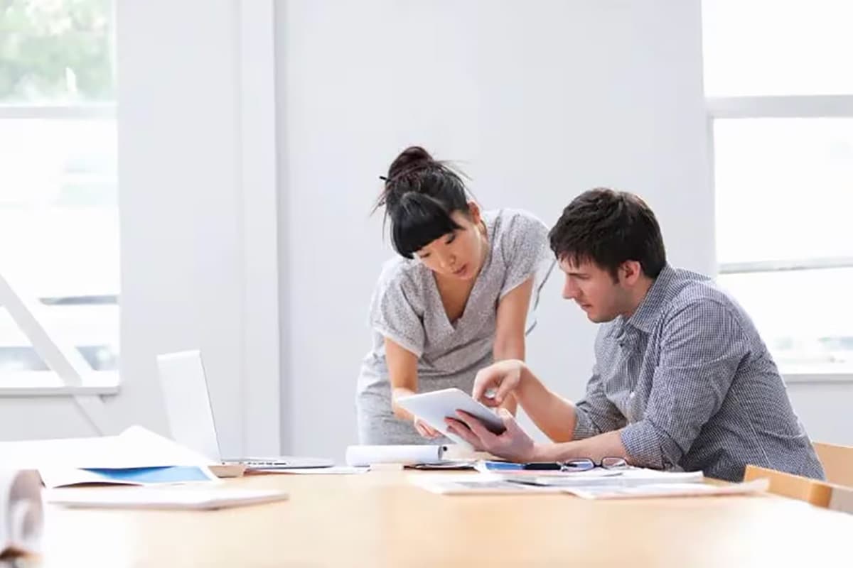 Two colleagues collaborate over a laptop in a modern office, discussing credit card definitions and types.