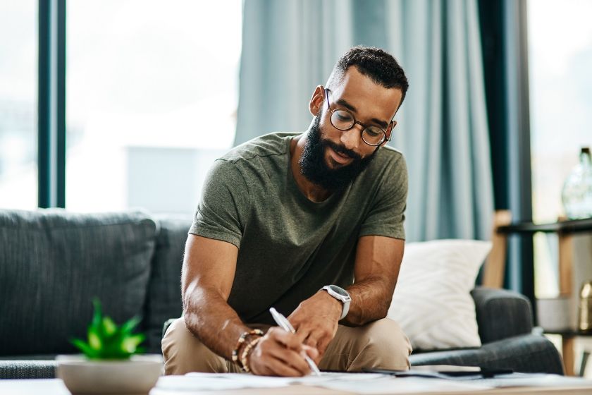 Man reviewing paperwork concerning debt settlement while sitting on couch