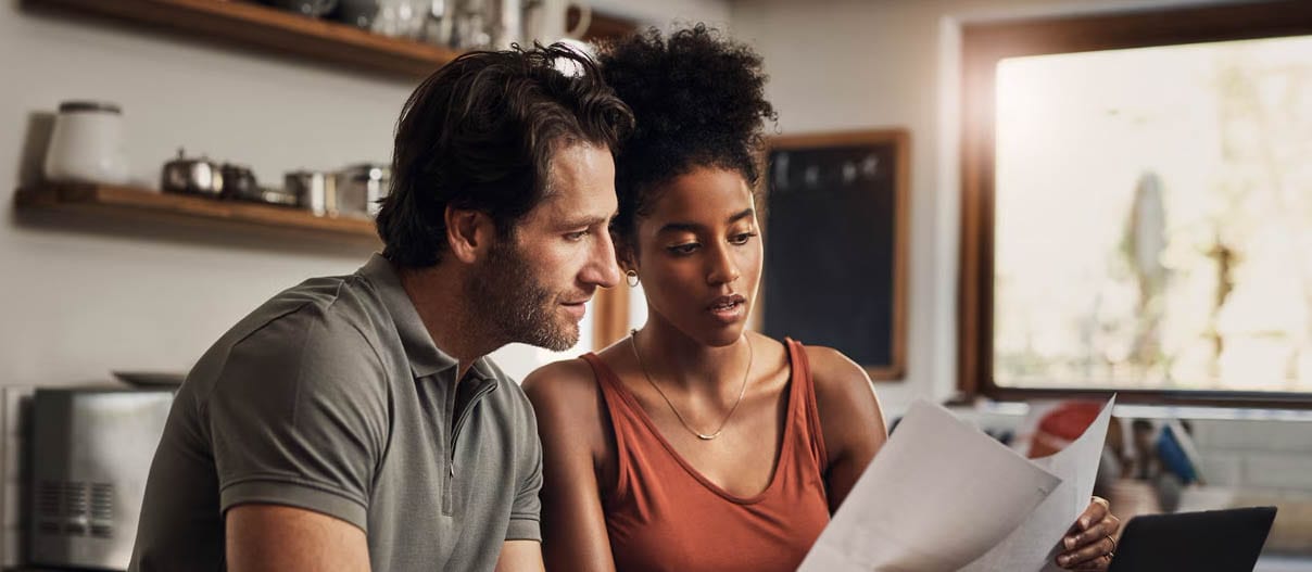 A couple reviews financial documents together in their kitchen, discussing their debt-to-income ratio and calculations.