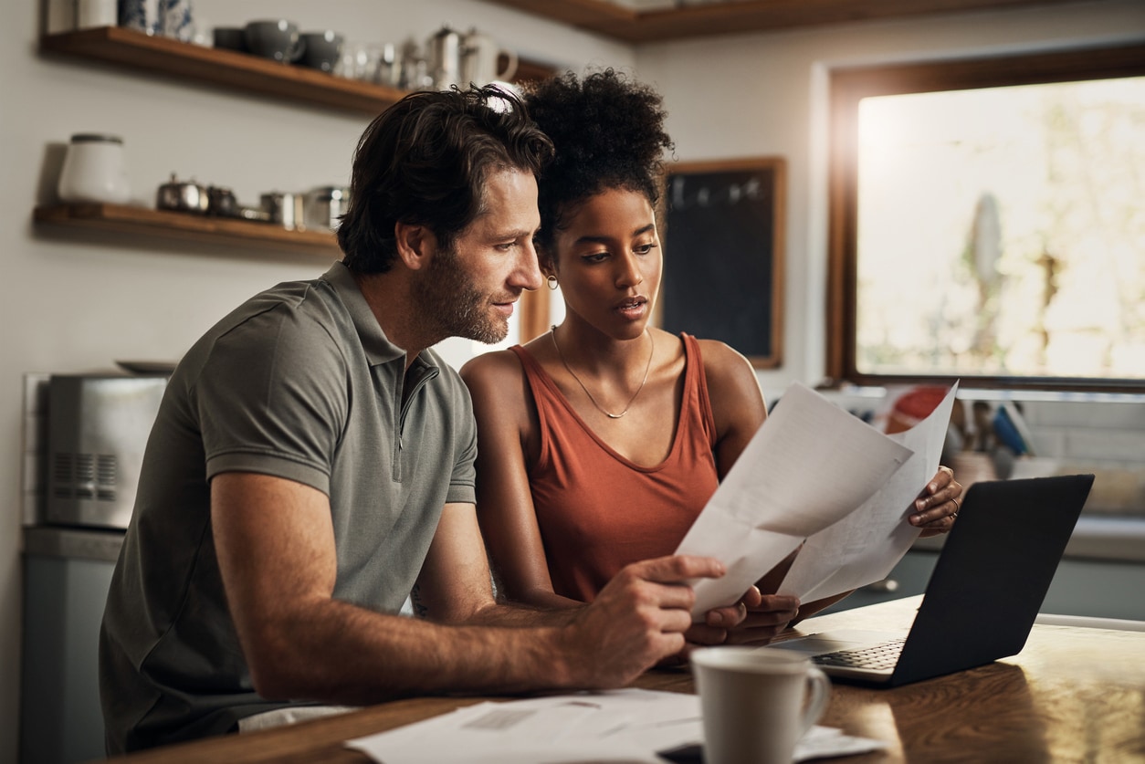 A couple reviews financial documents together in their kitchen, discussing their debt-to-income ratio and calculations.