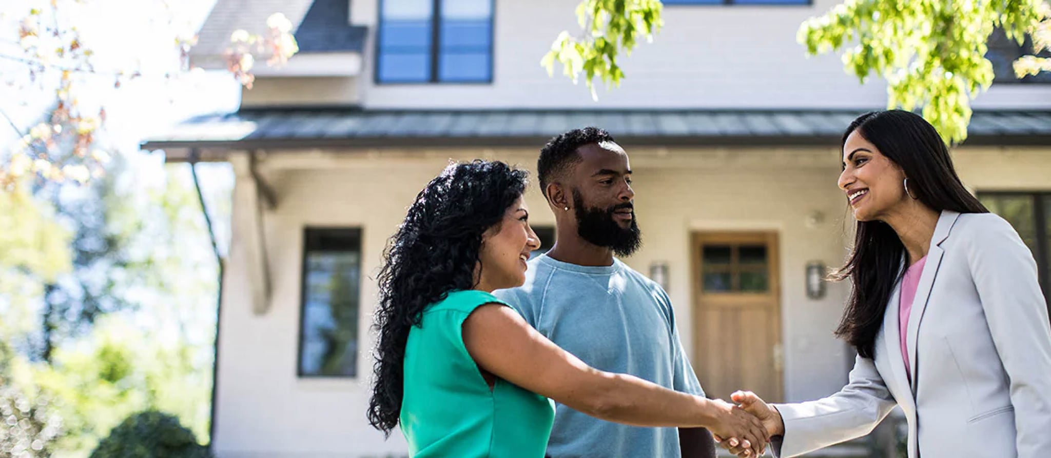 A couple shaking hands in front of a house, symbolizing a successful real estate transaction and the escrow process.