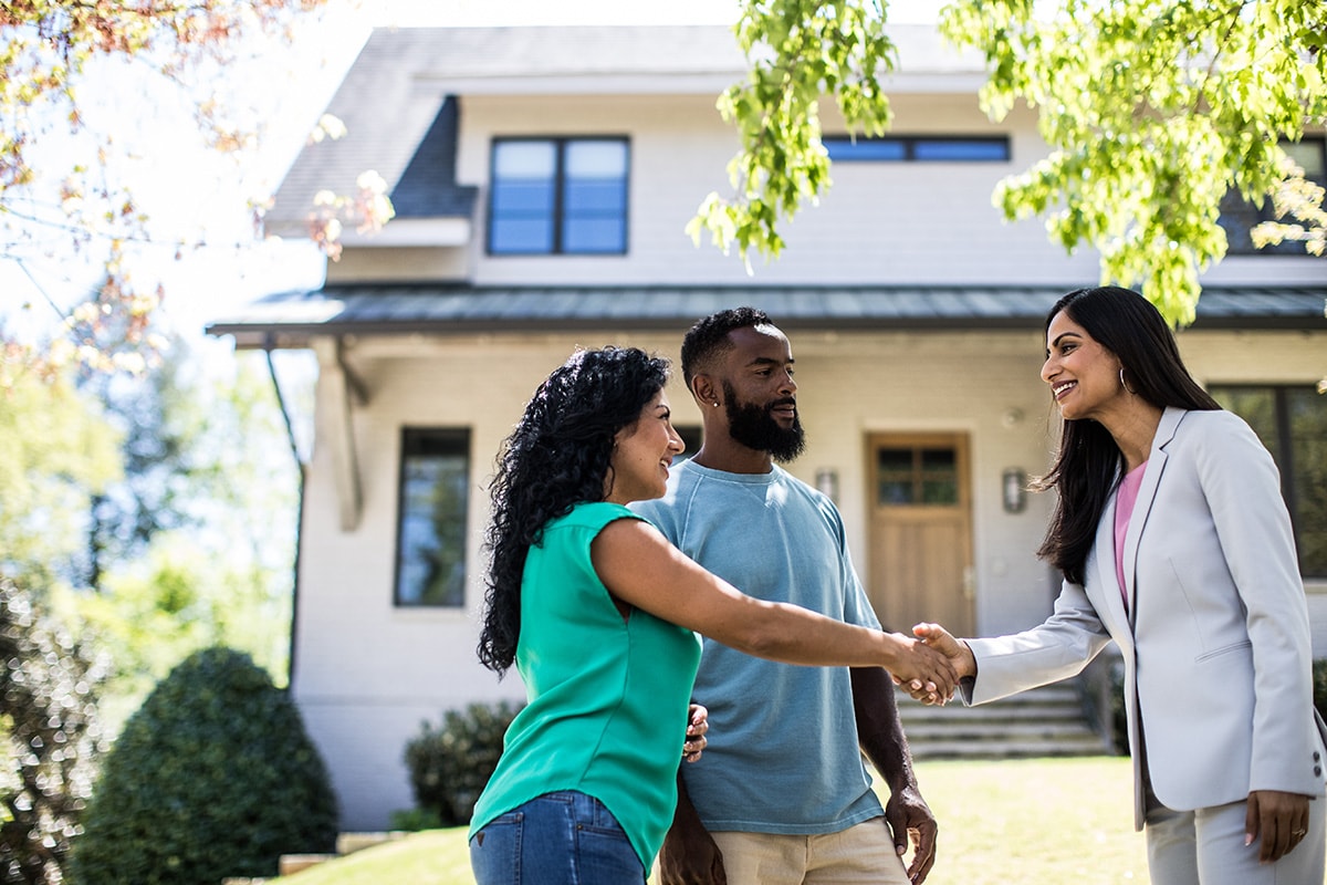 A couple shaking hands in front of a house, symbolizing a successful real estate transaction and the escrow process.
