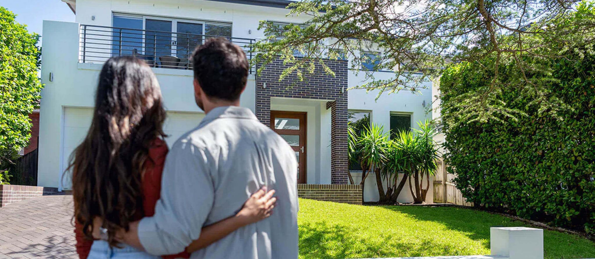A couple stands together in front of their house, symbolizing the concept of home equity and its potential benefits.