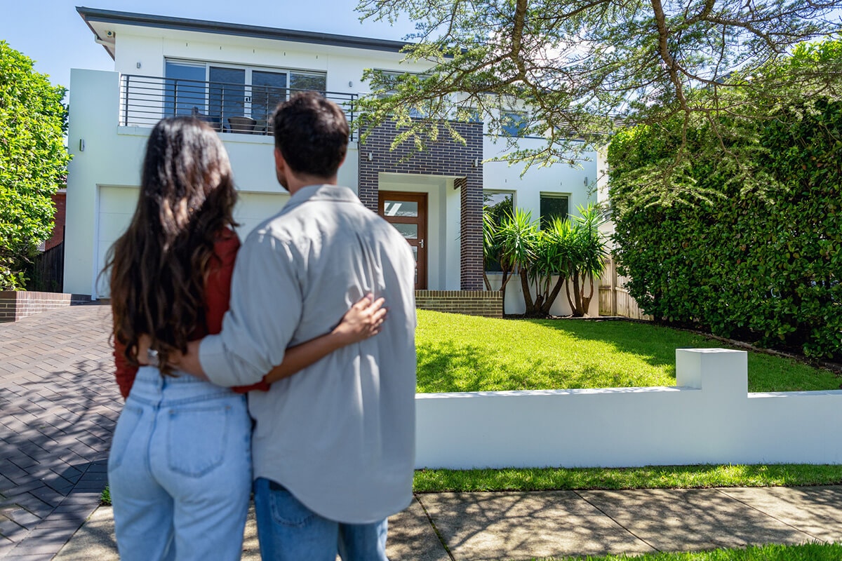 A couple stands together in front of their house, symbolizing the concept of home equity and its potential benefits.