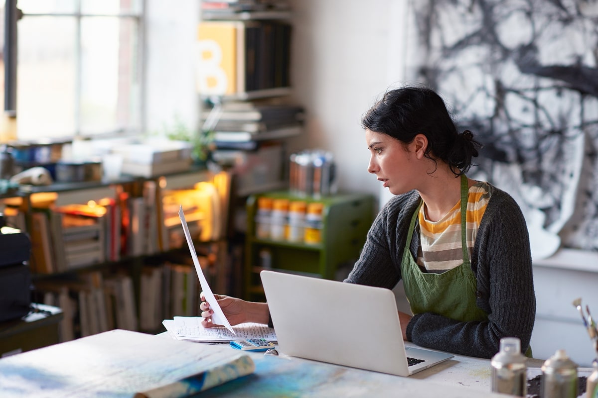 A professional image of a person reviewing their credit card statement on a laptop, with a calculator and notebook nearby.