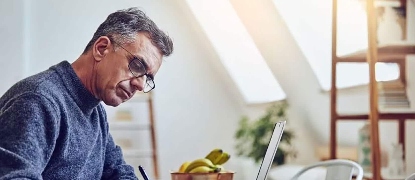 A man writes in a pad that is next to his laptop while sitting at his desk