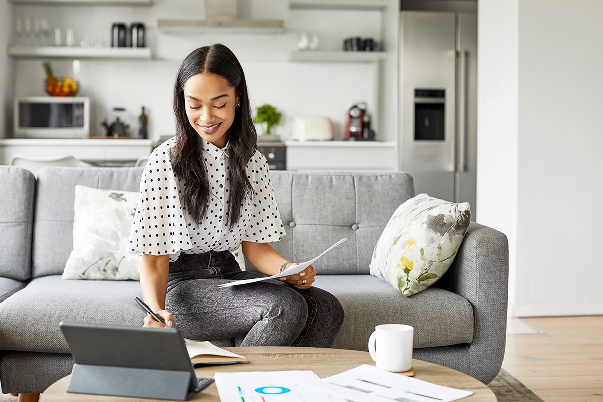 A woman is sitting and working on a laptop on a sofa.