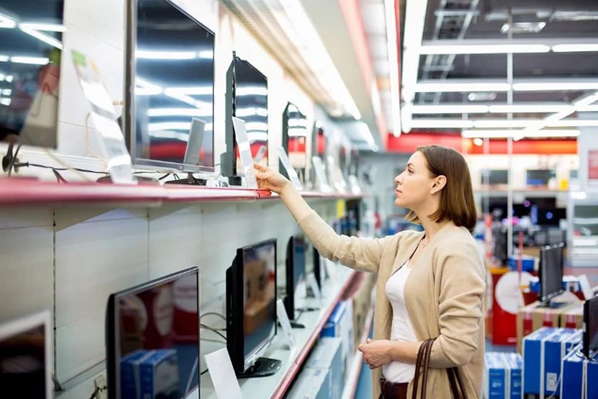 A woman examines a television display in a store, contemplating her options for a potential purchase.
