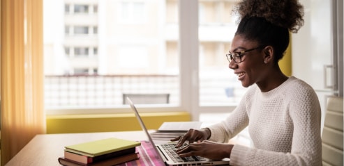 Woman in home office smiling at her laptop while seated at desk