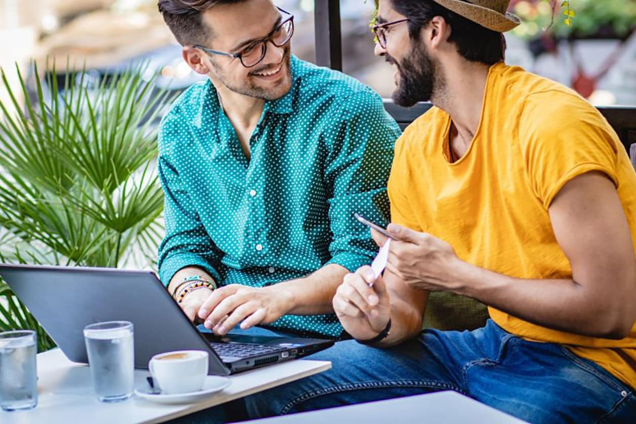Two men sitting at a table with a laptop and smiling
