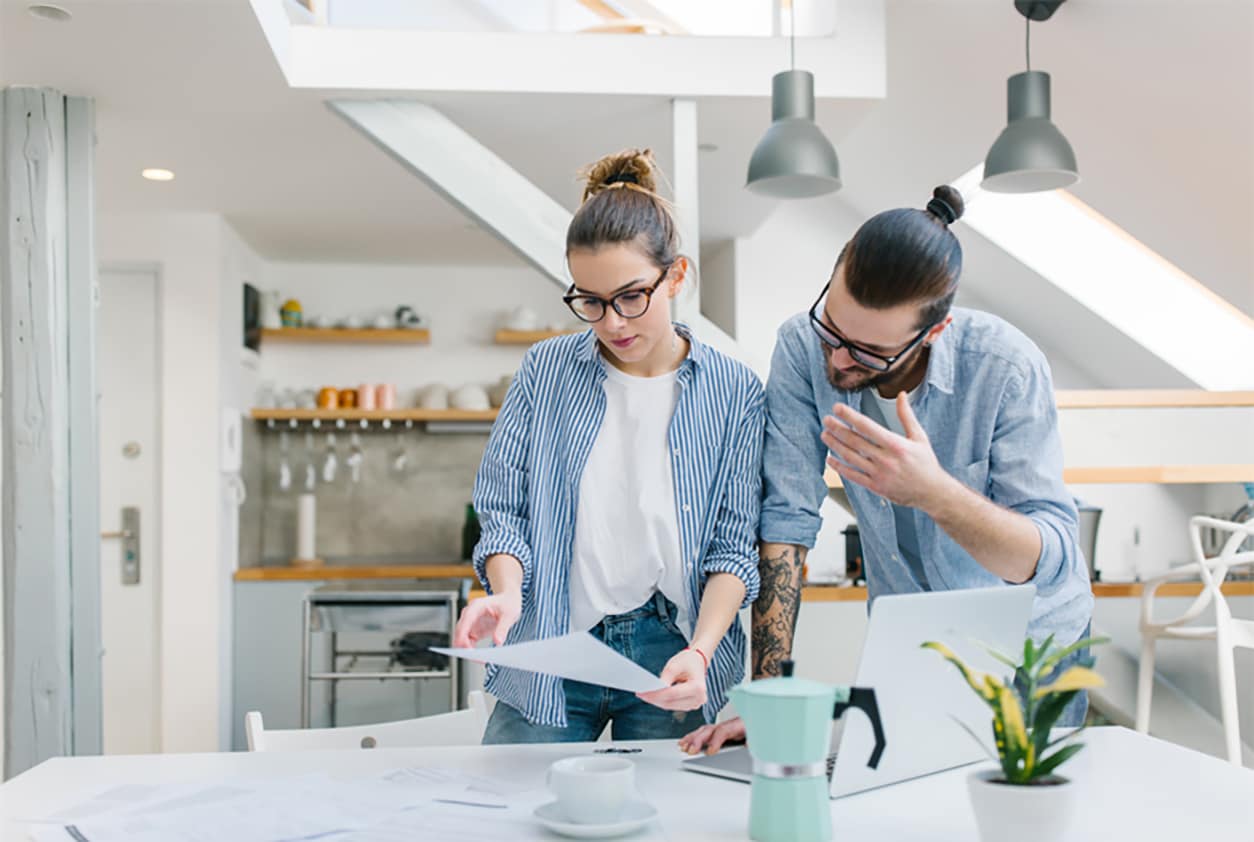 A man and a woman standing over a dining room table while looking over some papers