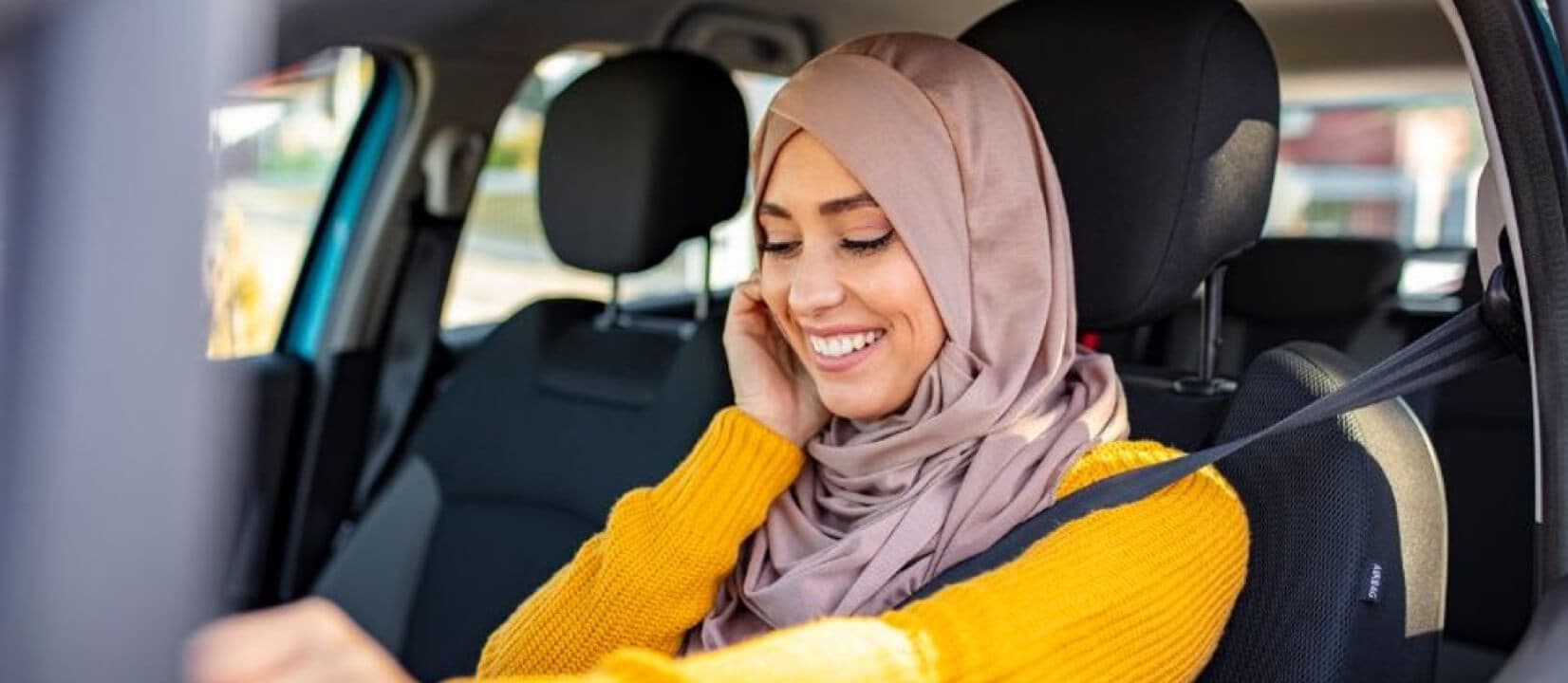 A woman speaks on her phone while sitting in her car