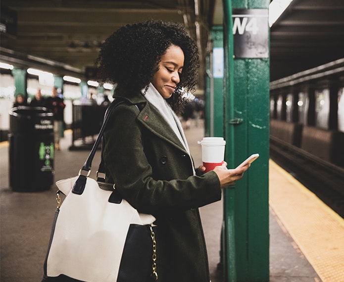 Woman holding coffee looking at phone while waiting for subway.