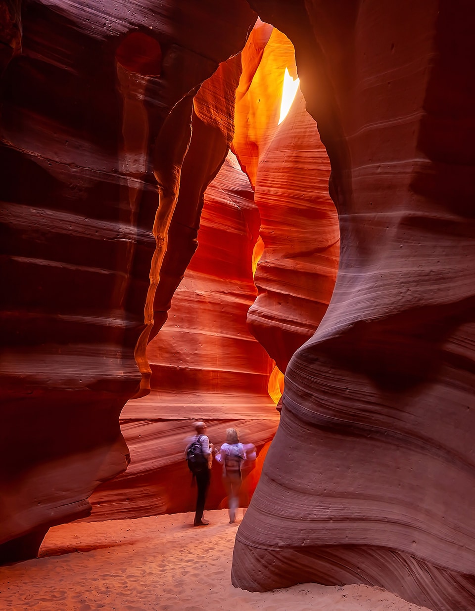 Dos excursionistas caminando por un cañón de arenisca roja iluminado por la luz del sol