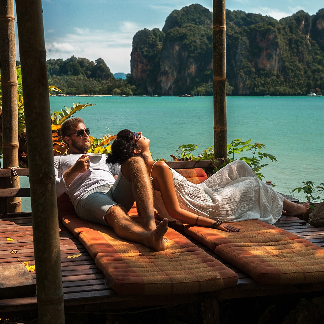 Pareja descansando en una terraza de madera con vistas al mar turquesa y acantilados tropicale