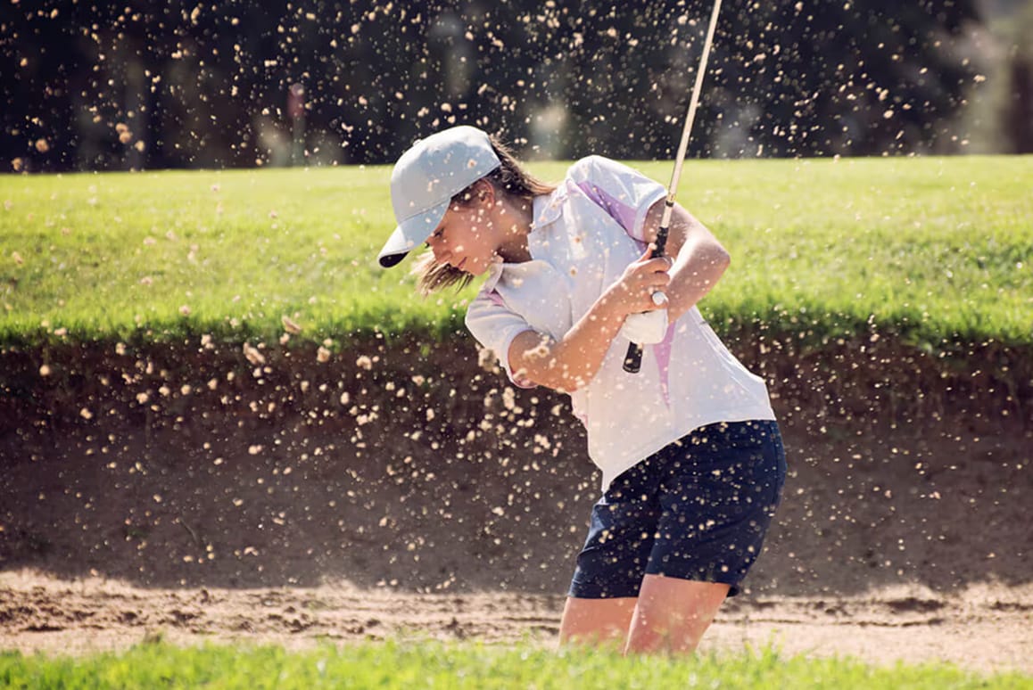 Mujer golpeando una pelota de golf desde un búnker de arena