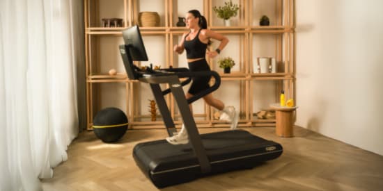 Promoción Hot Sale de Technogym con AMEX: mujer ejercitándose en caminadora premium para entrenamiento en casa con hasta 6 meses sin intereses en equipo fitness.