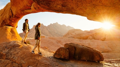 Una mujer y un hombre en un paisaje desértico durante la puesta de sol.