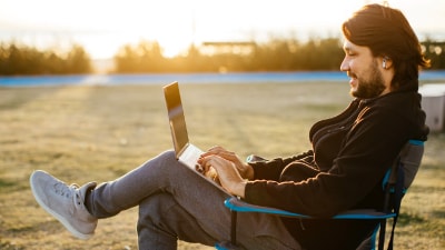 Un hombre con una laptop sentado en una silla en el campo.
