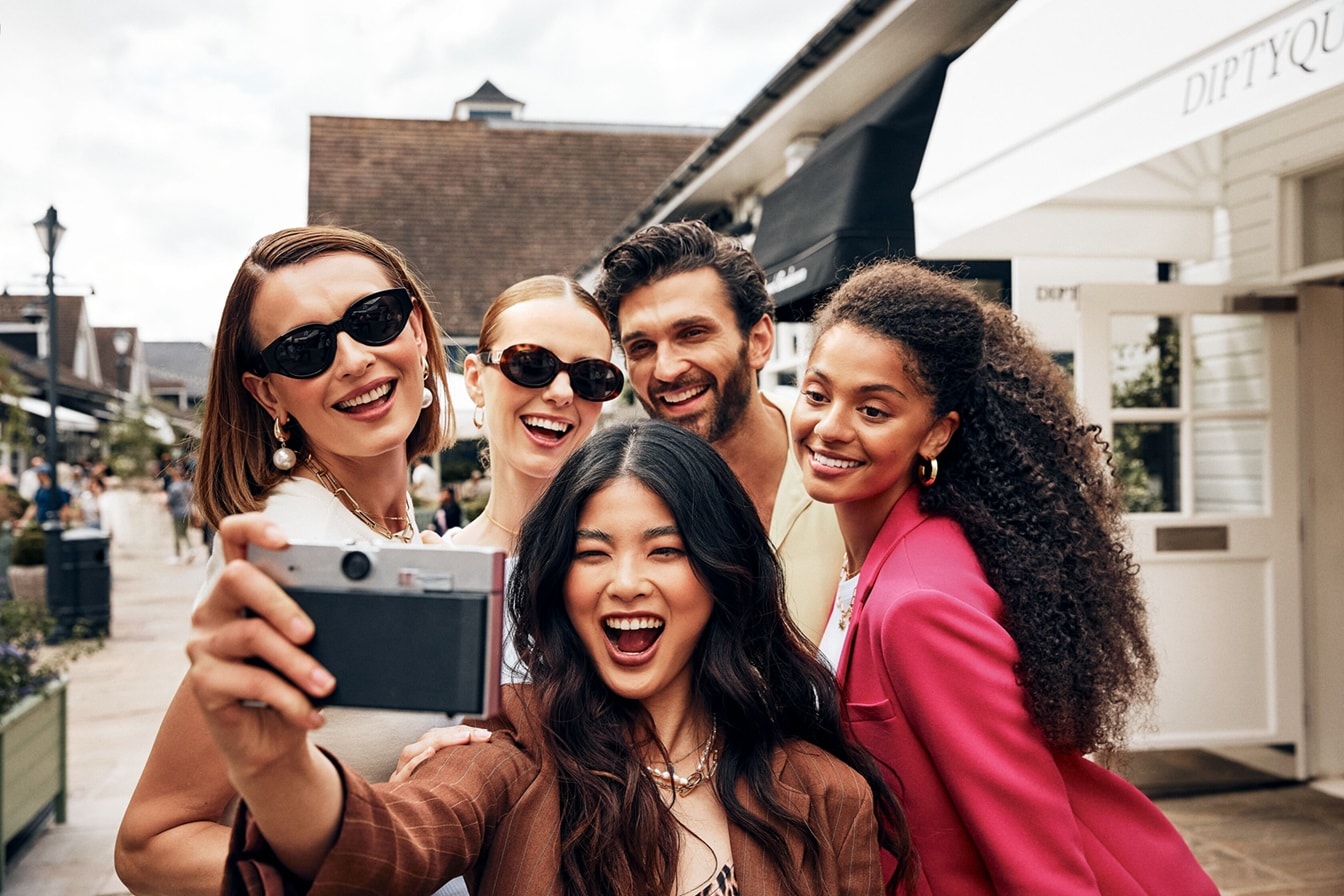 Un grupo de cuatro mujeres y un hombre sonriendo hacia una cámara – AMEX MX