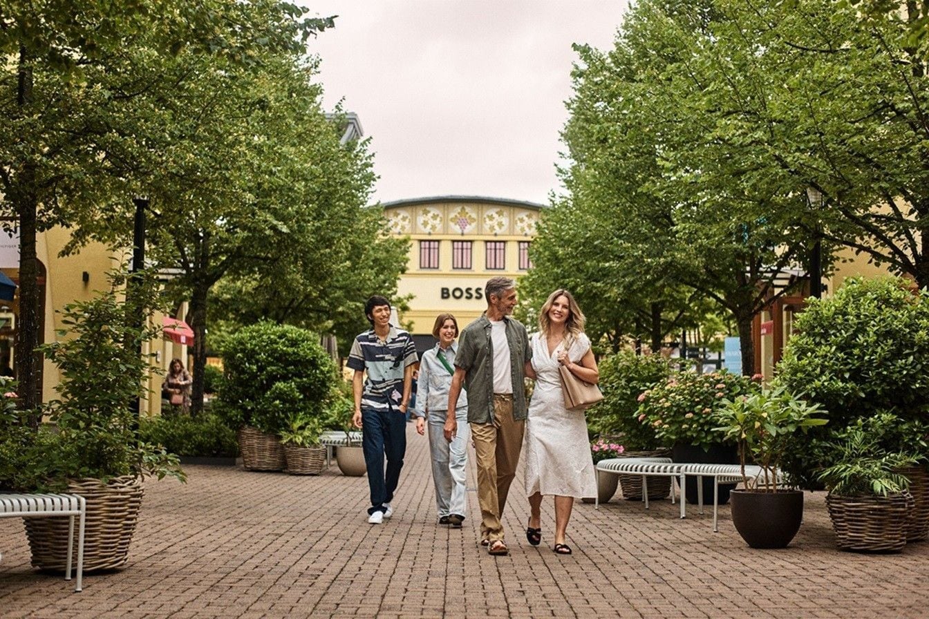 Una mujer y hombre sonriendo y caminando rodeados de árboles, y detrás de ellos hay una pareja caminando – AMEX MX