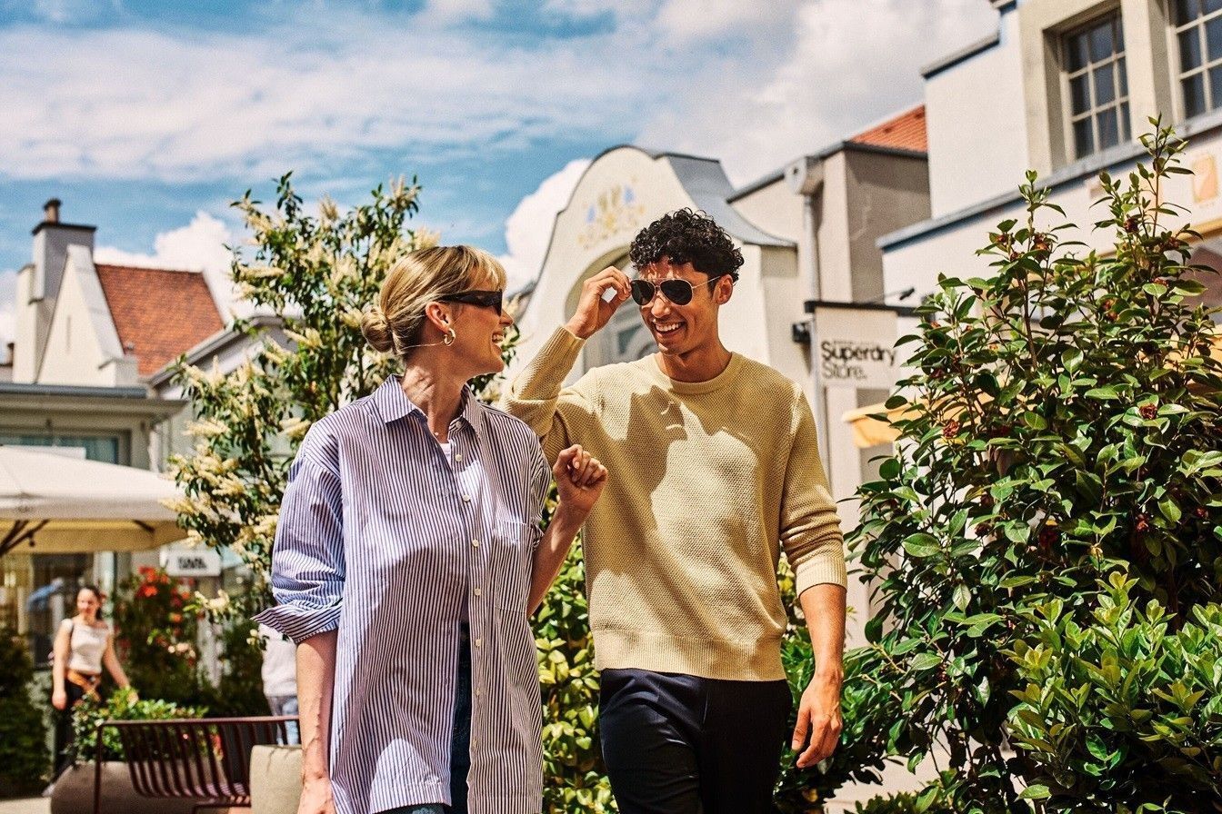Una mujer y un hombre con lentes de sol caminando hacia el frente sonriendo – AMEX MX