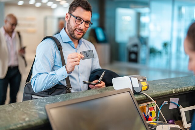 Un hombre registrándose en la recepción de un hotel, mostrando una tarjeta American Express.