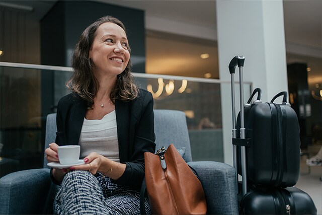 Una mujer tomando un café en una sala VIP de un aeropuerto, junto a su maleta.