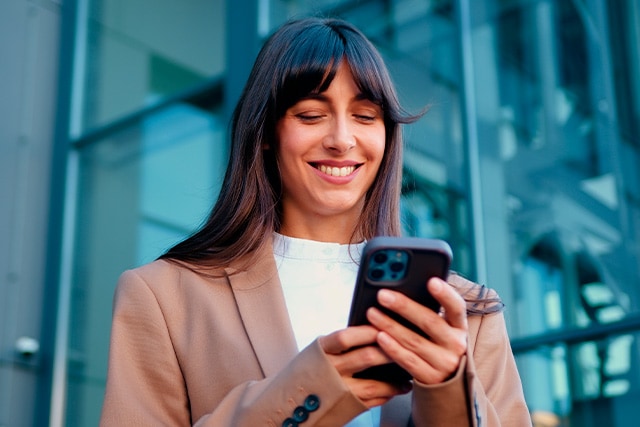 Mujer sonriendo mientras mira su teléfono celular.