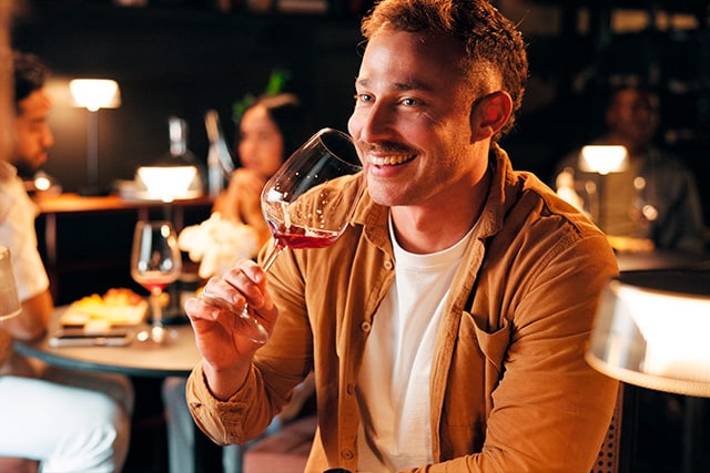Un joven sonriente bebiendo vino en un restaurante elegante.