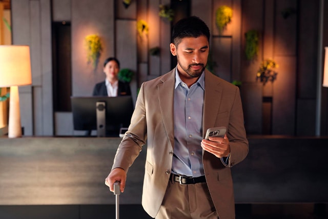 Un hombre de negocios con traje alejándose de la recepción de un hotel revisando su teléfono.