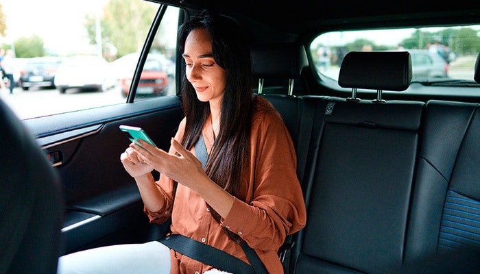 Una mujer sentada en la parte trasera de un taxi revisando su teléfono.