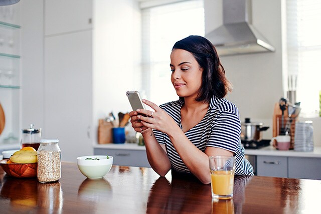 Una mujer con su celular en la mesa de la cocina.