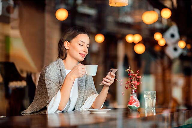 Mujer disfrutando de una taza de café y revisando su teléfono celular.