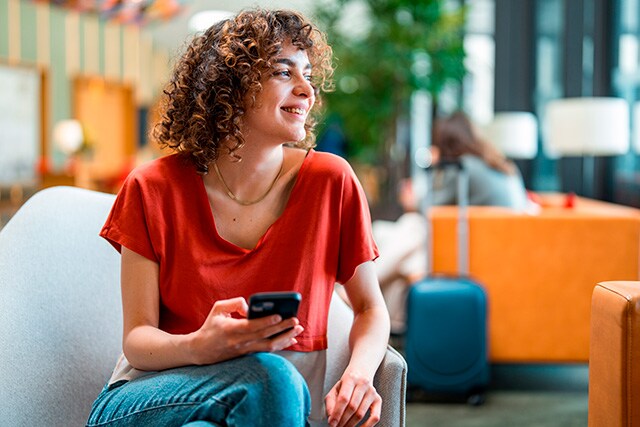 Mujer revisando su celular en una sala de espera de un aeropuerto.