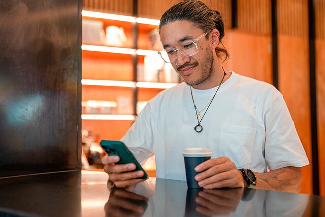 Un joven revisando su teléfono celular mientras toma un café.