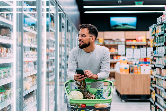 Un hombre haciendo la compra y revisando su teléfono celular.