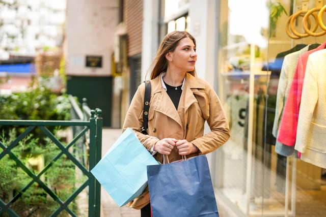 Mujer joven con una bolsa de compras mirando el escaparate de la tienda.